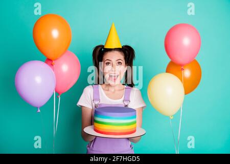 Photo de fille folle tenir le gâteau de chercher l'espace vide les ballons portent une couleur bleu sarcelle isolée avec un chapeau de cône en papier violet arrière-plan Banque D'Images