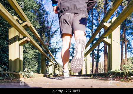 vue arrière d'un jeune coureur traversant un parc boisé en bas d'une passerelle en bois dans le concept sportif de printemps ou d'été soins personnels Banque D'Images