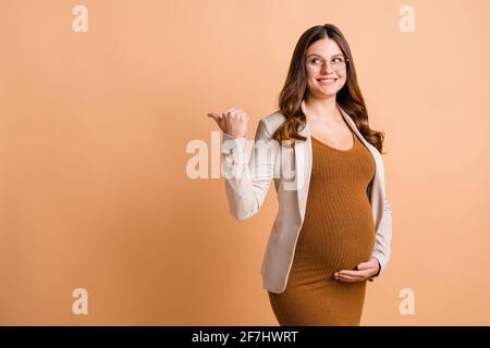 Photo d'une jolie femme brillante s'attendant à porter une veste d'enfant pointant pouce vers le haut, l'arrière-plan beige est isolé dans un espace vide Banque D'Images