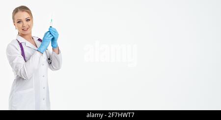 Une jeune infirmière dans un masque et un manteau blanc tient une seringue avec une aiguille pour les injections, les vaccins contre la grippe, le covid. Le concept de vaccination et de protection Banque D'Images