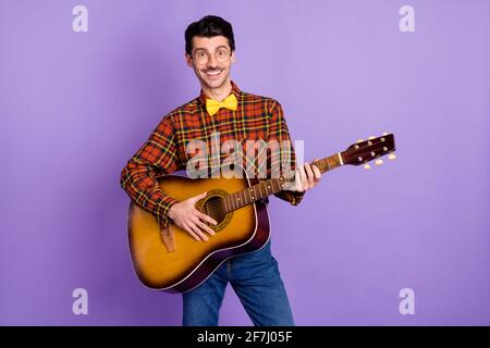 Photo de jeune beau positif gai romantique homme jouant acoustique guitare sur date isolée sur fond violet Banque D'Images