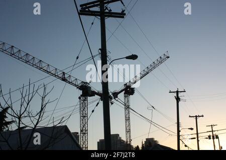 Silhouettes de grues, de poteaux et de fils dans le sud de Vancouver, en Colombie-Britannique, au crépuscule Banque D'Images