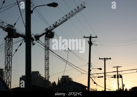 Silhouettes de grues, de poteaux et de fils dans le sud de Vancouver, en Colombie-Britannique, au crépuscule Banque D'Images