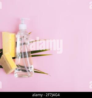 Poser à plat avec une feuille de palmier verte, un compte-gouttes de savon, du liquide vaisselle, du savon à vaisselle, un débarbouillette sur fond rose pastel et jaune. Photo de haute qualité Banque D'Images