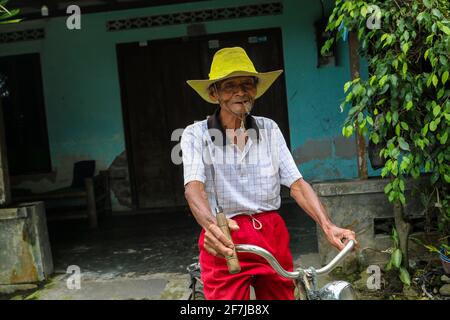 Un portrait d'un vieil agriculteur indonésien porte un chapeau jaune avec vieux vélo Banque D'Images