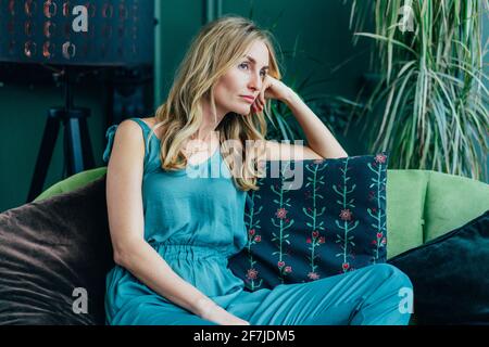 Jeune blond caucasien attrayant est assis ennuyé sur le canapé. Personne rêveuse pensive. Portrait de mode d'une femme. Banque D'Images