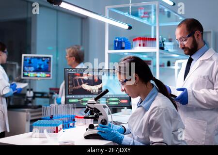 Femme scientifique analysant le virus au microscope en laboratoire de chimie de recherche avec équipe. Médecin et chimistes qui font l'examen de l'évolution du vaccin, travaillant au développement du diagnostic. Banque D'Images