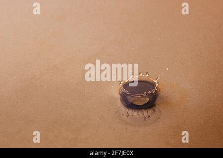 Une éclaboussure sur la surface lisse de l'eau à travers laquelle vous pouvez voir le fond sablonneux. Image d'arrière-plan Banque D'Images