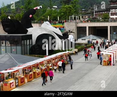 (210408) -- CHENGDU, 8 avril 2021 (Xinhua) -- les touristes visitent un marché créatif à côté de la sculpture de 'Sefie Panda' sur la place Yangtianwo à Dujiangyan, dans le sud-ouest de la Chine, dans la province du Sichuan, le 7 avril 2021. Création de l'artiste néerlandais Florentijn Hofman, la sculpture a une dimension de 26,5 m sur 11 m sur 12 m, avec un panda géant à prise de selfie couché sur le dos. Pesant 130 tonnes, le travail prend forme à l'aide de trois millions de tiges en acier inoxydable peintes en laque. « Seelfie Panda » s'inspire d'un véritable panda géant qui s'est égaré dans le centre-ville de Dujiangyan en 2005. Il est rapidement devenu un phot populaire Banque D'Images