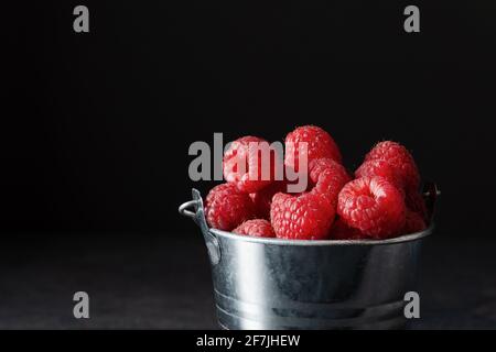 Framboises mûres fraîches dans un petit seau en métal sur fond noir. Framboise juteuse pleine de vitamines. Banque D'Images