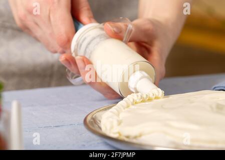 femme boulangère tire la crème fouettée. Gâteau aux fraises fait maison à base de gâteau meringue et de crème aux fraises. Banque D'Images