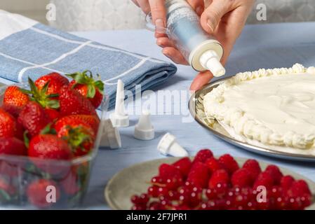 femme boulangère tire la crème fouettée. Gâteau aux fraises fait maison à base de gâteau meringue et de crème aux fraises. Banque D'Images