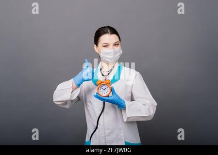Belle femme médecin dans le masque protecteur regardant loin et pensant à quelque chose. Banque D'Images