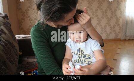 Une jeune mère attentionnée embrasse son bébé contrarié, embrassant sur le front. Photo de haute qualité Banque D'Images