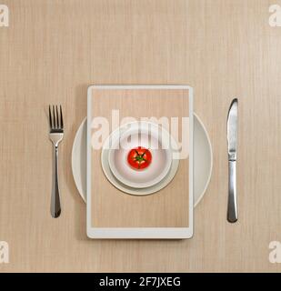 Commande en ligne d'une tomate dans une assiette, sur un écran de tablette. Technologie d'alimentation numérique. Service personnel. Banque D'Images