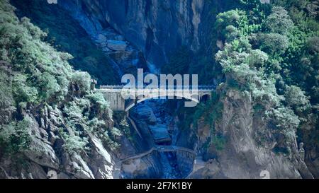 Un vieux pont en pierre au pied de la montagne avec des arbres verts dans la gorge du tigre bondissant de Lijiang. Banque D'Images