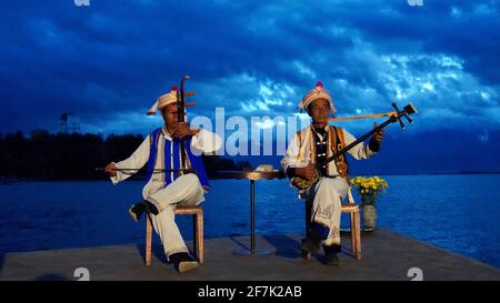 Deux hommes plus âgés s'habillant avec les gens traditionnels de Bai et Jouer des instruments de musique par Erhai lac avec nuageux et bleu tonifie le ciel pendant la nuit Banque D'Images