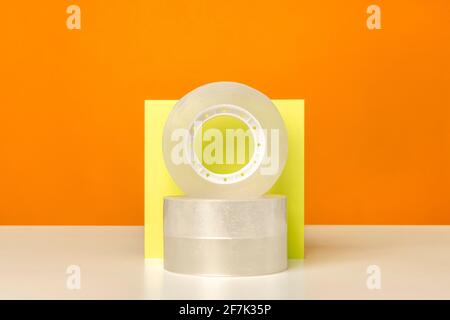 Coller le ruban adhésif sur la table blanche sur fond orange vif. Couleurs minimalistes et vives. Fournitures de bureau. Banque D'Images