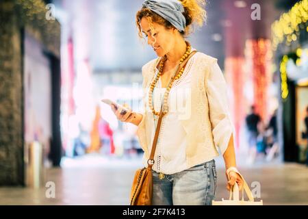 Les gens utilisent le téléphone cellulaire dans le centre commercial - gai joli femme adulte envoyant un message texte sur un smartphone pendant une activité de magasinage - moderne femme tendance cl Banque D'Images