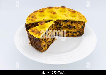 Gâteau traditionnel au simnel maison avec une tranche coupée Une assiette blanche pour Pâques - gâteau aux fruits recouvert de garniture et boules de massepain grillé jaune Banque D'Images