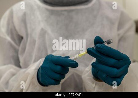 Médecin remplissant la seringue avec le vaccin Corona, Covid-19, mains en gants de caoutchouc et manteau blanc, gros plan. Banque D'Images