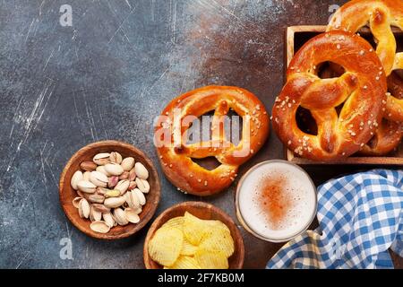 Tasse à bière lager, noix, chips de pomme de terre et bretzel maison frais cuit avec sel de mer sur table en pierre. Collation classique à la bière. Vue de dessus plat avec bac à papier Banque D'Images