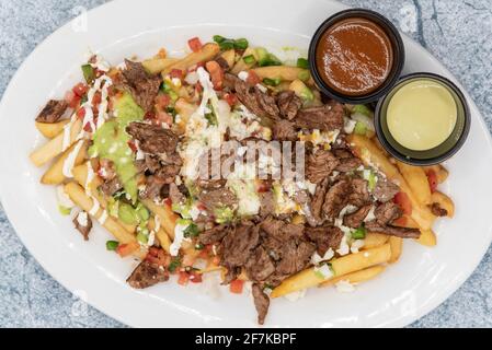 La vue sur le dessus d'une grande assiette de frites Asada, recouvertes de fromage et servies avec une sauce à trempette, séduira tout le monde. Banque D'Images