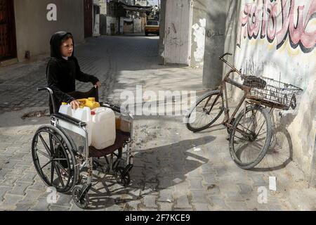 08 avril 2021, Territoires palestiniens, Rafah : un enfant palestinien pousse un fauteuil roulant avec des jerricans remplis d'eau potable au camp de réfugiés de Rafah. Le nouveau gouvernement américain, sous la présidence de Joe Biden, veut réintroduire le soutien aux Palestiniens arrêté par l'ancien président Donald Trump. Le Département d'État a déclaré mercredi que 150 millions de dollars devaient d'abord être versés à l'Office de secours et de travaux des Nations Unies (UNRWA) pour l'aide humanitaire, et que 75 millions de dollars d'aide au développement étaient destinés à des projets dans la bande de Gaza et en Cisjordanie. Photo: Abed Rahim Khatib/dpa Banque D'Images