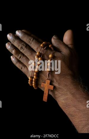 Main de prière d'un vieil homme catholique indien avec rosaire en bois isolé sur un fond noir Uni. Banque D'Images