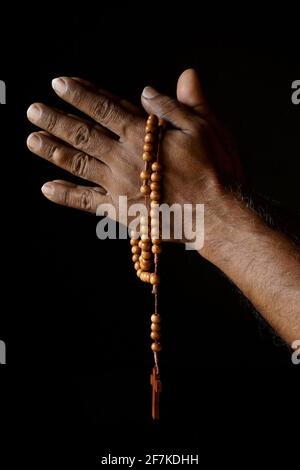 Main de prière d'un vieil homme catholique indien avec rosaire en bois isolé sur un fond noir Uni. Banque D'Images