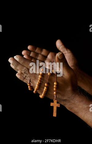 Main de prière d'un vieil homme catholique indien avec rosaire en bois isolé sur un fond noir Uni. Banque D'Images