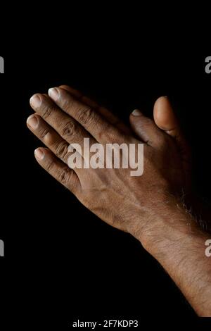 Priant les mains de l'homme catholique indien isolé sur un fond noir. Banque D'Images