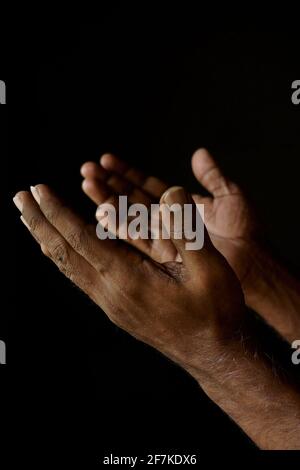 Priant les mains de l'homme catholique indien isolé sur un fond noir. Banque D'Images