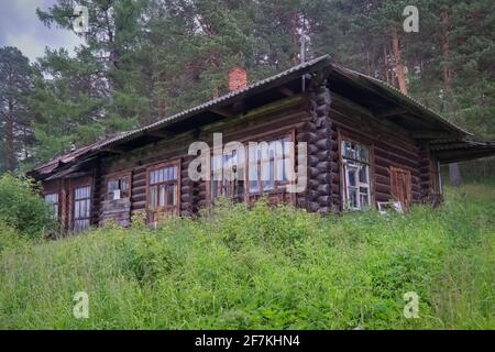 Maison en bois en rondins en ruine abandonnée solitaire vieille et dépassée, surcultivée avec de l'herbe dense et des buissons dans la forêt. Banque D'Images