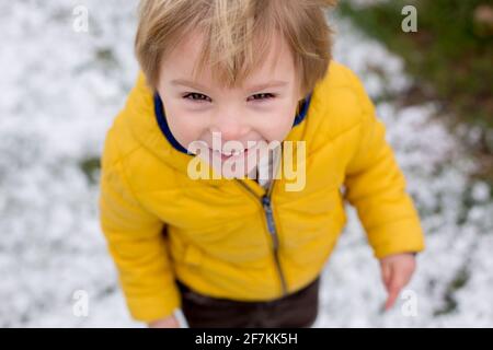 Mignon blond enfant, garçon, courir autour de la fleur de brousse jaune, temps de printemps, tout en neige, le temps de printemps inhabituel avec de la neige Banque D'Images