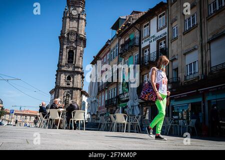 Porto, Portugal. 07e avril 2021. Une femme portant un masque de visage marche alors qu'en arrière-plan on voit des gens assis sur une esplanade juste en face de la Tour Clerigos. La deuxième phase du processus de déconditionnement au Portugal a débuté le 5 avril. Les restaurants et les cafés-restaurants ont été autorisés à accueillir des personnes sur les tables en plein air par groupes de 4 par table et les gens peuvent maintenant se promener dans la ville avec plus de liberté. (Photo par Teresa Nunes/SOPA Images/Sipa USA) crédit: SIPA USA/Alay Live News Banque D'Images