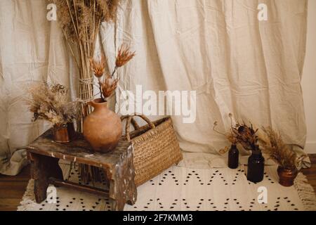 Décoration de style bohème. Fleurs de protea sèches dans vase d'argile, pampas herbe, panier en osier, tapis sur fond de beige cl Banque D'Images