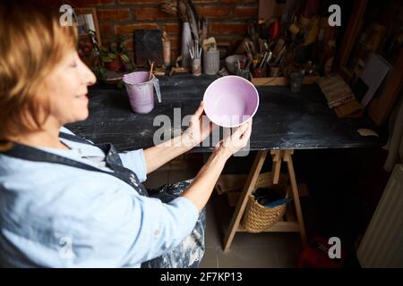 Femme artiste en céramique tenant un bol peint dans un atelier de poterie Banque D'Images