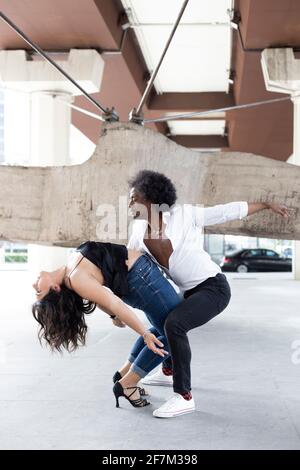 Jeune couple multiethnique exécutant magistralement une figure de danse compliquée. Ils sont à l'extérieur. Espace pour le texte. Banque D'Images