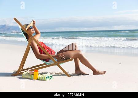 Femme de course mixte sur la plage de vacances assis dans le transat de bains de soleil Banque D'Images