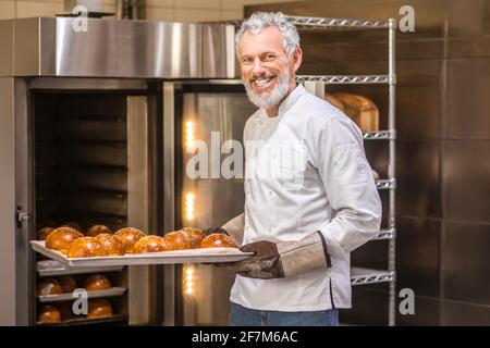 Homme en gants avec plateau de petits pains fraîchement cuits Banque D'Images