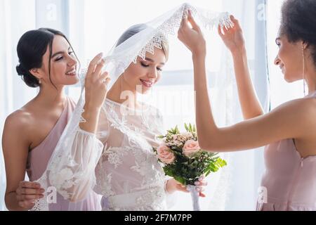 femme afro-américaine levant le voile de la mariée tenant le bouquet de mariage Banque D'Images