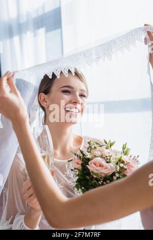 demoiselle d'honneur tenant le voile de la mariée joyeuse avec le bouquet de mariage et champagne Banque D'Images