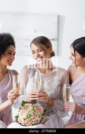 les demoiselles d'honneur multiculturelles qui cherchent une mariée heureuse tout en tenant des verres à champagne Banque D'Images