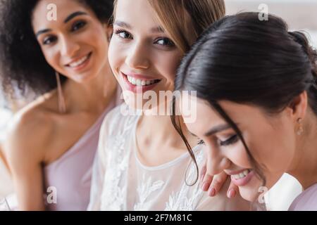 mise au point sélective de jeunes mariés souriant à l'appareil photo près de l'interracial les bridesmaides Banque D'Images