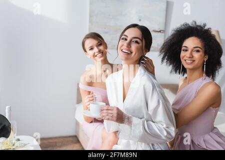 une femme heureuse avec des demoiselles d'honneur interraciales souriant à l'appareil photo dans la chambre Banque D'Images