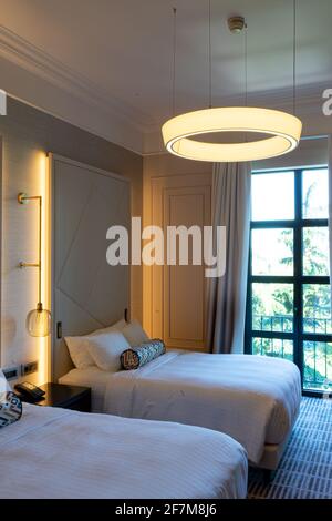 Chambre luxueuse avec deux lits, literie et linge blanc frais dans un intérieur moderne, sous la lampe ronde jaune Banque D'Images