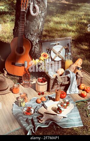 Panier pique-nique vintage, panier avec baguette et limonade à l'extérieur sur une herbe avec fromage, mozzarella, tomates, cerises, vigne. Guitare, en-cas Banque D'Images