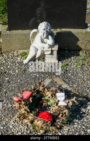 Une statue d'un chérubin à ailes découragées surplombe un flétrit Couronne de Noël sur une tombe dans un cimetière irlandais Banque D'Images