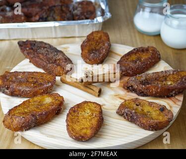 Torrijas espagnoles maison traditionnelle faisant un cercle et trois cannelle bâtons au milieu sur une plaque ronde en bois décorée avec ses ingrédients a Banque D'Images